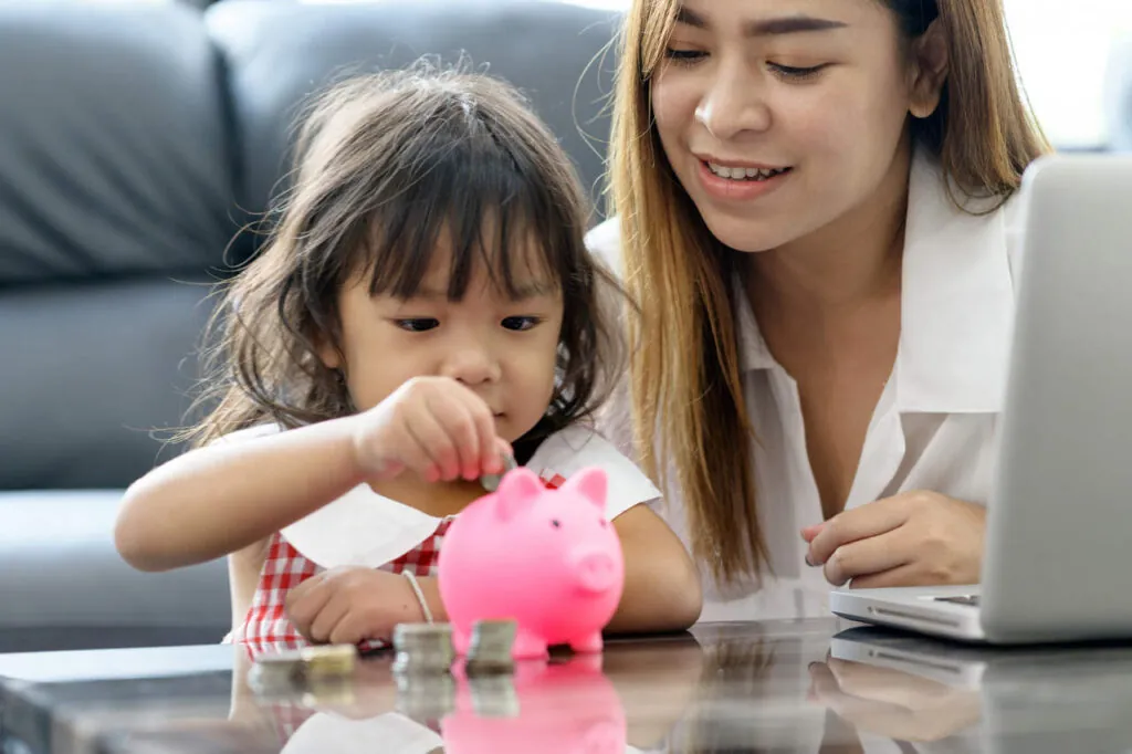 mãe com filha pequena colocando dinheiro em cofre porco