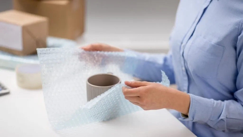 Como embalar móveis para mudança: mulher envolvendo uma xicara em plástico bolha.