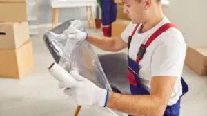 Como embalar móveis para mudança: Homem com rolo de plástico bolha na mão embalando um objeto.