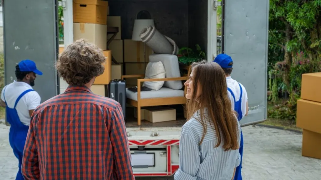Profissionais descarregando caminhão de mudança enquanto casal olha.