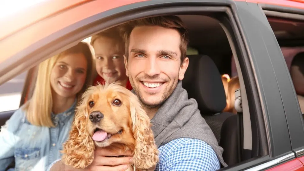 como transportar cachorros em carros: família em carro com cachorro no colo de tutor.